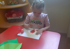 Kornelka maluje biedronkę z talerzyka papierowego.